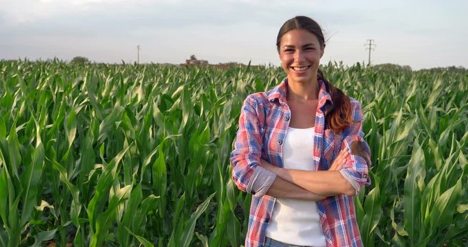 Beautiful girl (woman) farmer smiling, looking, checking cornfield, young tanned, green background. Concept: ecology, corn, bio product, inspection, water, natural products, professional, environment.