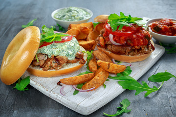 Delicious Bagel Pork sandwiches with vegetable and Tzatziki Sauce and Fries on white board.
