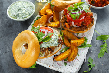 Delicious Bagel Pork sandwiches with vegetable and Tzatziki Sauce and Fries on white board.
