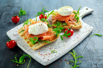 Poached egg on grilled toast with smoked salmon, rucola and vegetables on white board. healthy breakfast