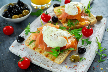 Poached egg on grilled toast with smoked salmon, rucola, olives, vegetables and orange juice. on white board. healthy breakfast