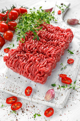Fresh Raw Beef Minced Meat with salt, pepper, chilli and fresh thyme on white board.