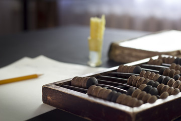 Abacus with candle, book and balance sheet on dark background