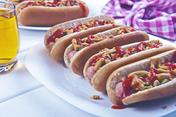 Hot dogs with roasted onion, pickled cucumber, ketchup and mustard on a white table