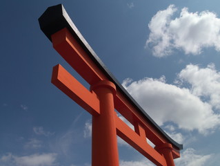 A japanese tor-ii against the blue sky with puffy clouds