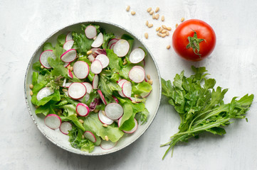 Healthy radish salad with lettuce mix, arugula and pine nuts on white background. Top view. 