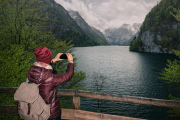 Germany. Berchtesgaden National Park.  A girl with a mobile phone on a viewing platform with a view of the lake Konigssee