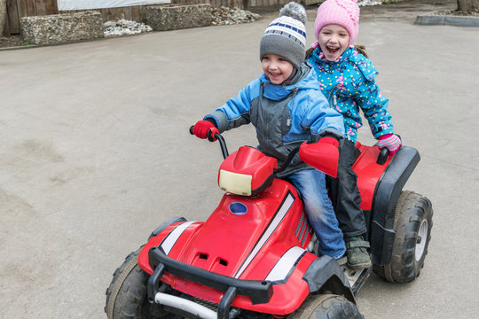 Boy girl children's ride on a double Quad bike. They are dressed in pants, jackets and caps.