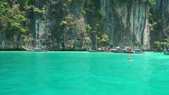 Krabi cliff contrast with green turquoise ocean of Thailand. Lot of tourist boat parking around bay area