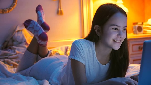 Beautiful teenage girl having night conversation through online messenger on laptop