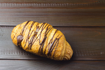One sweet croissant with chocolate on dark brown wooden table