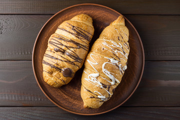 Two sweet croissant at plate of clay on dark brown wooden table, top view