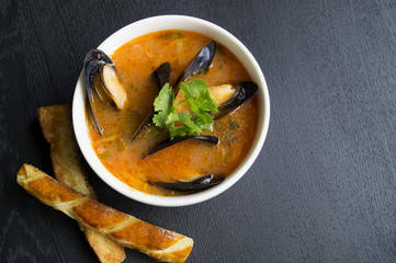 Tomato soup with mussels. With fried croutons on a black background.