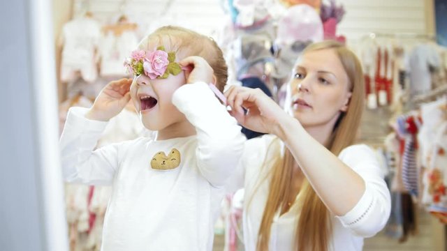 Child's dress store - little blonde baby girl doing shopping and buying pretty hat