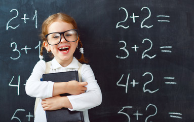 Happy schoolgirl preschool girl with book near school blackboard