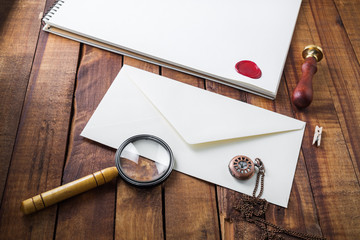 Photo of blank paper envelope, magnifier, seal, stamp and clock on wooden table background....