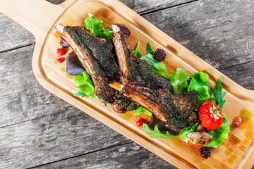 Grilled lamb ribs in herbs and greens, fresh salad, grilled vegetables and berries on cutting board on wooden background
