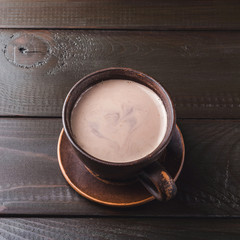 Hot chocolate or cocoa drink in clay cup, on dark brown wooden table