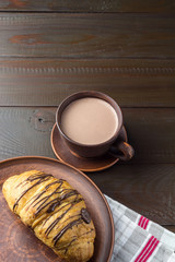 Hot chocolate or cocoa drink in cup and sweet croissant at plate on napkin, dark brown wooden table
