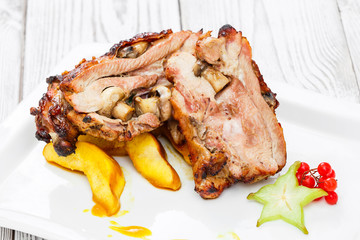 Roasted pork stuffed with mushrooms, peach, carambola, cranberries and sweet sauce on plate on wooden background close up