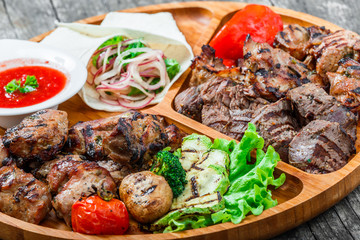 Assorted delicious grilled meat and vegetables with fresh salad and bbq sauce on cutting board on wooden background close up