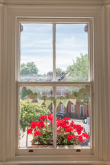 Interior of a Victorian British house with old wooden white windows  and red geranium flowers on the window sill facing a traditional English street
