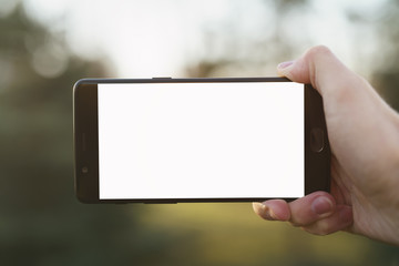 man right hand holding smartphone with white screen outdoors with spring blurred background, shallow focus