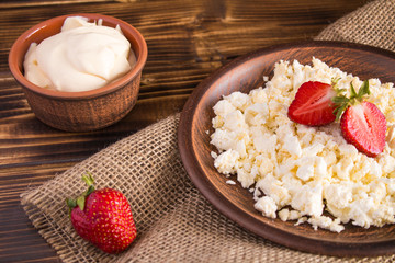 Cottage cheese with strawberry and sour cream in the brown plate on tne wooden background