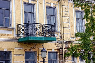 Старый открытый балкон на фасаде здания заросший растениями