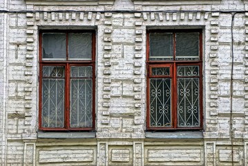 Старые разбитые окна  с решёткой на кирпичной стене здания