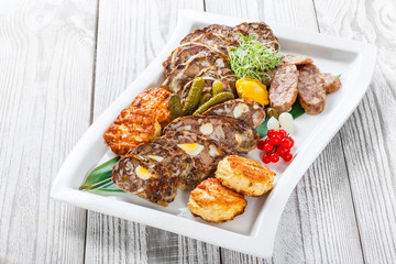 Juicy delicious meat cutlets and homemade sausage with pickled vegetables on plate on wooden background. Meat appetizer