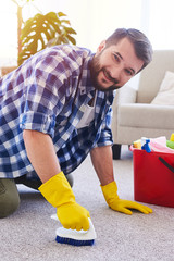 Hardworking sir in gloves brushing carpet