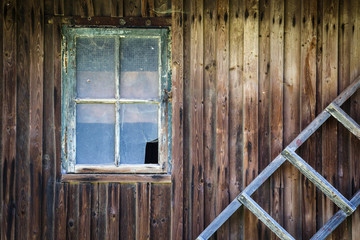 Old broken window in the wooden wall of the house and old wooden ladder