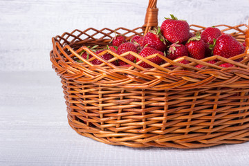 Fototapeta na wymiar Wicker basket filled with ripe strawberries. On a white wooden background.