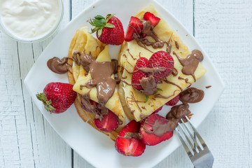 Pancakes with strawberries drizzled with chocolate. On a white wooden background. The view from the top.