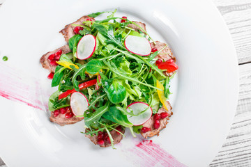 Salad with beef steak, baby spinach, lettuce, sweet pepper and grains of pomegranate on wooden background close up. Top view