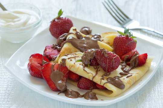 Pancakes with strawberries drizzled with chocolate. On a white wooden background.