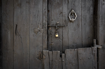 ancient dark brown wooden door with a door knocker a padlock and a bolt
