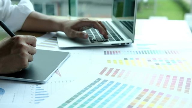 young male graphic designer working with computer and color swatch. creative man using stylus pen and digital tablet at modern office. Architect using work tools and sample colour catalog. business, t