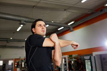 Fototapeta na wymiar Young sporty man in the black sportwear stretching arm before gym workout.