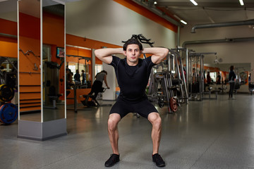 Naklejka na ściany i meble Portrait of young sportsman in the black sportwear while making squat in gym.