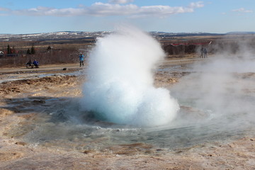 A jet of water and air is violently forced out through the hole in the rocks.