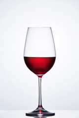 Elegant crystal wine glass with red wine against light background with reflection.