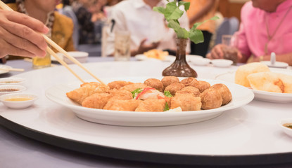 Fried food on dining table with hand holding chopsticks to pick up in restaurant.