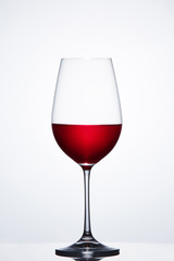 Red wine in the fragile pure wineglass standing against light bckground with reflection.