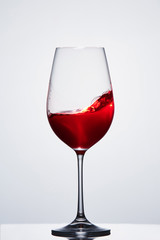 Red wine in a crystal pure wineglass showing waves against light background.