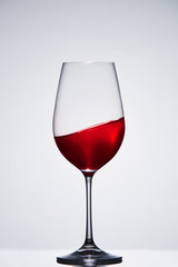 Wave of red wine in a crystal pure wineglass standing against light background with reflection.