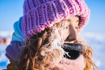 Close-up of a girl in a yellow down jacket pink knitted cap with red hair beautiful young hair in a...
