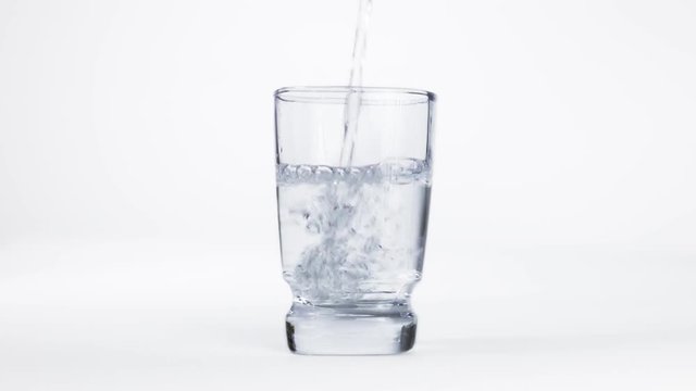 Pure and cold water is pouring into a transparent glass and creating bubbles and drops
