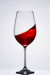 Wave of the romantic drink red wine on the pure wineglass standing against light background with reflection.